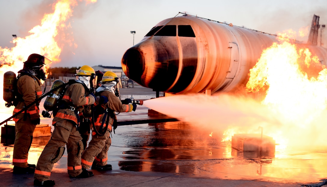 Airman approaches an exterior aircraft fire with a water hose during training