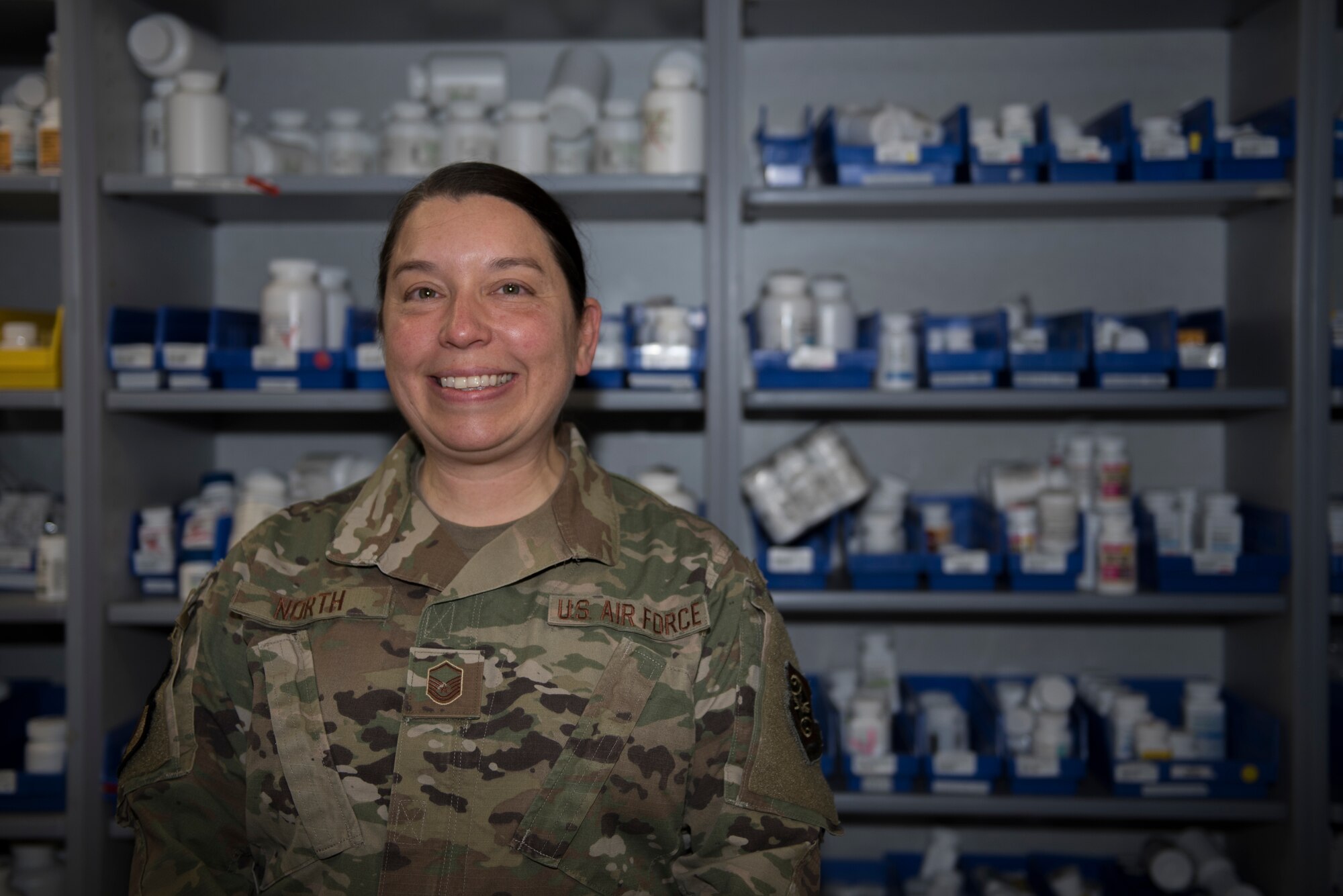 U.S. Air Force Master Sgt. Andrea North, 60th Medical and Diagnostics Therapeutic Squadron satellite pharmacy section chief, stands in front of the satellite pharmacy medicine wall Jan. 7, 2020, at Travis Air Force Base, California. North was recognized as the 60th Air Mobility Wing Warrior of the Week for her efforts in keeping the pharmacy running during a base power outage Nov. 27, 2019. The Warrior of the Week program recognizes Airmen who have made significant contributions to their unit. (U.S. Air Force photo by Airman 1st Class Cameron Otte)