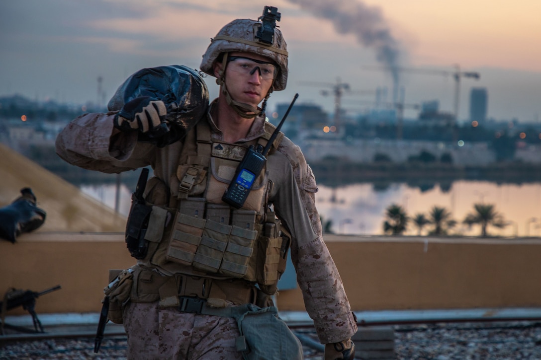 A combat-clad Marine carries a sandbag on his shoulder.