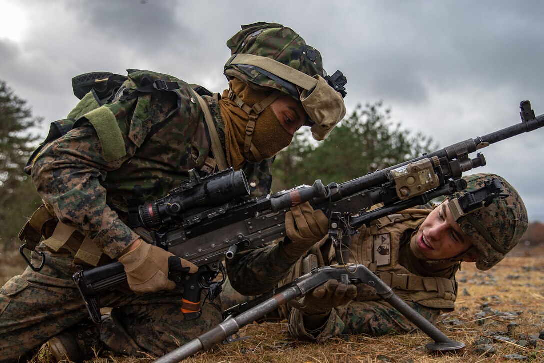 Two Marines set up a weapon system on the ground.