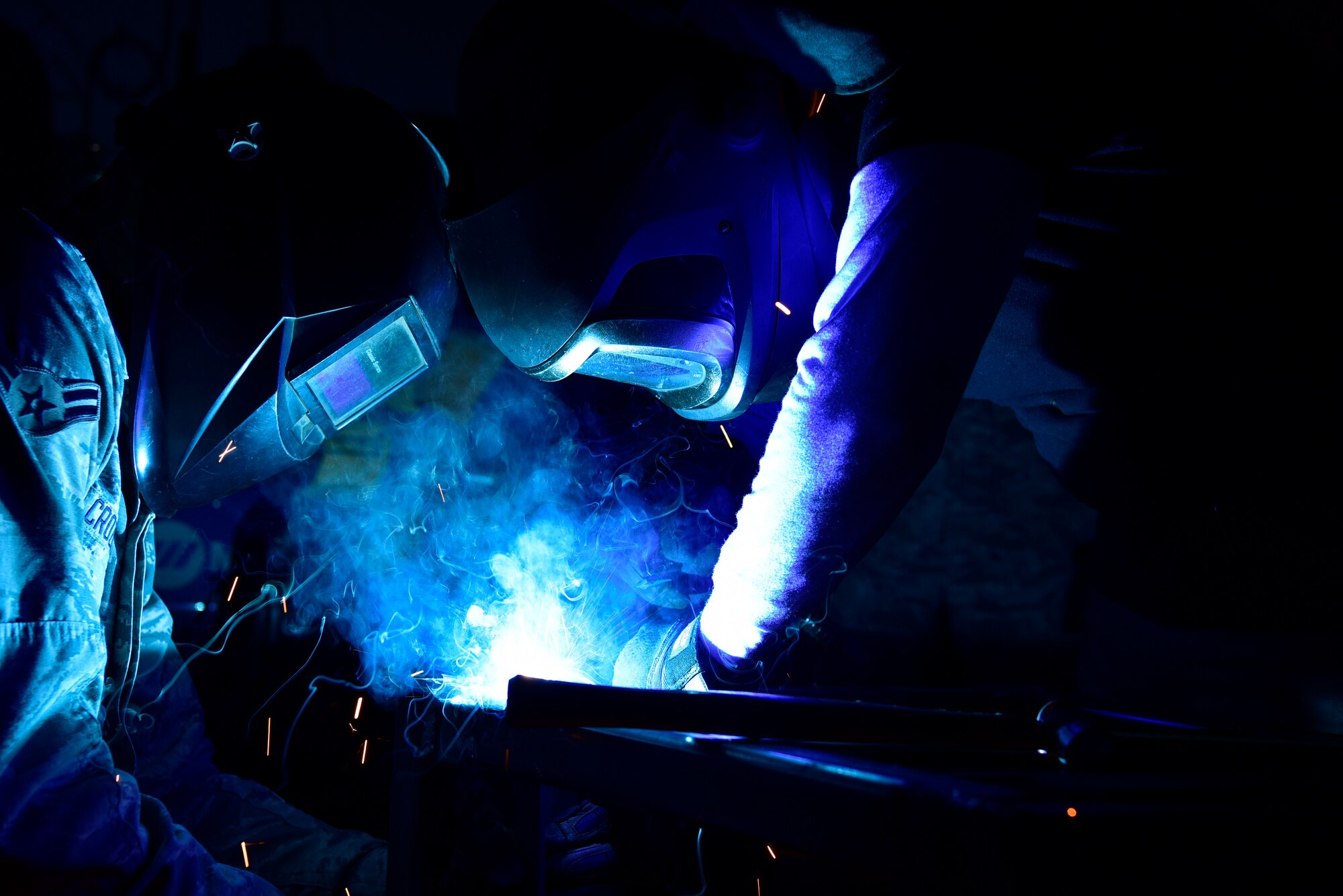 Airman apprentice, left, assists welder, as he welds a metal bar in place