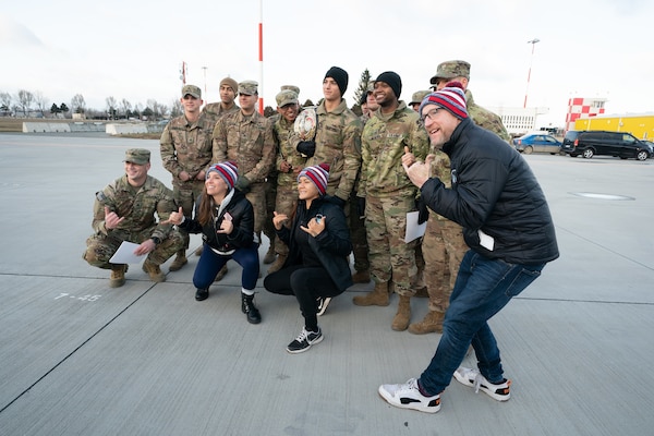 Service members pose with USO Tour participants on a flightline.