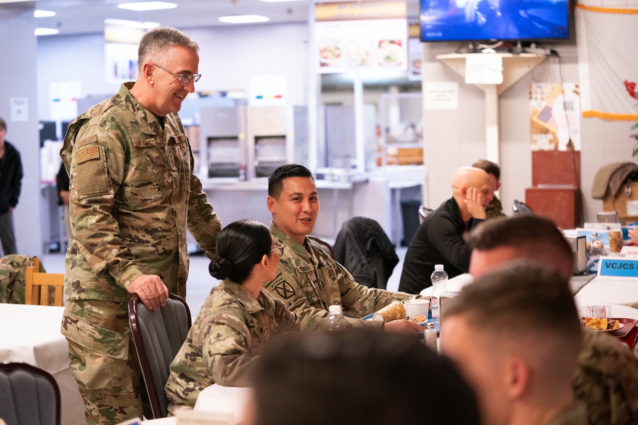 A military officer stands and speaks to a group of seated service members.