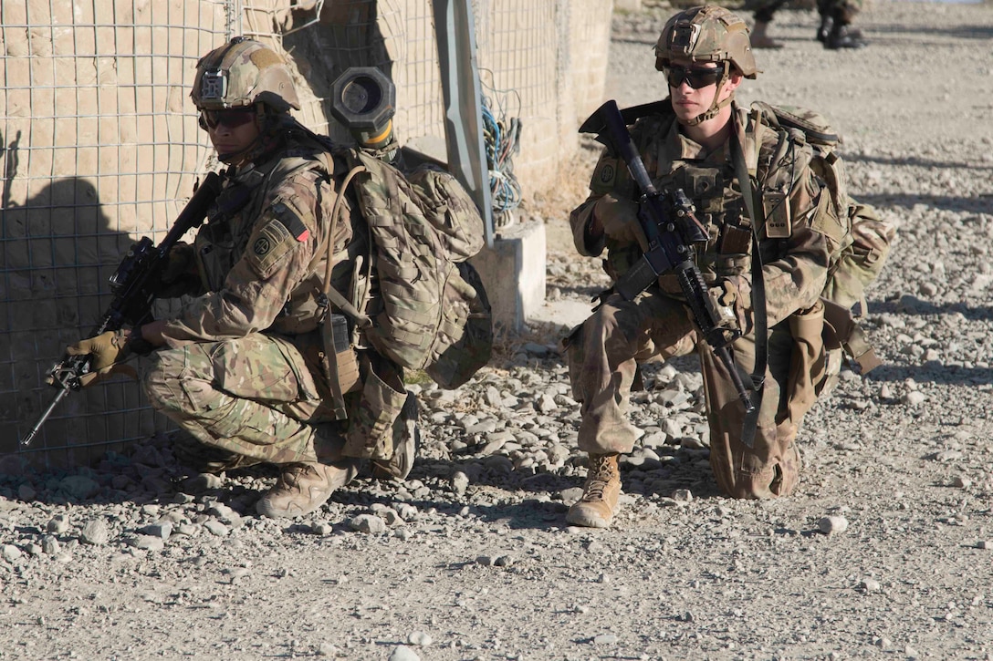 Two paratroopers carrying guns kneel on the ground.