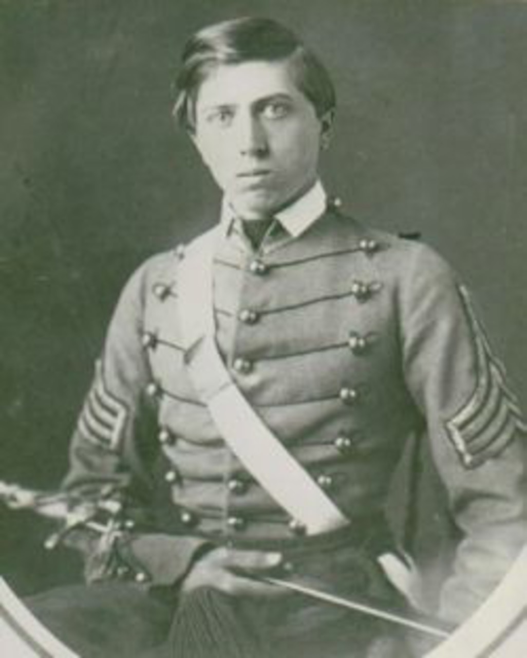 A young Civil War soldier in dress uniform looks at the camera as he holds a sword across his body