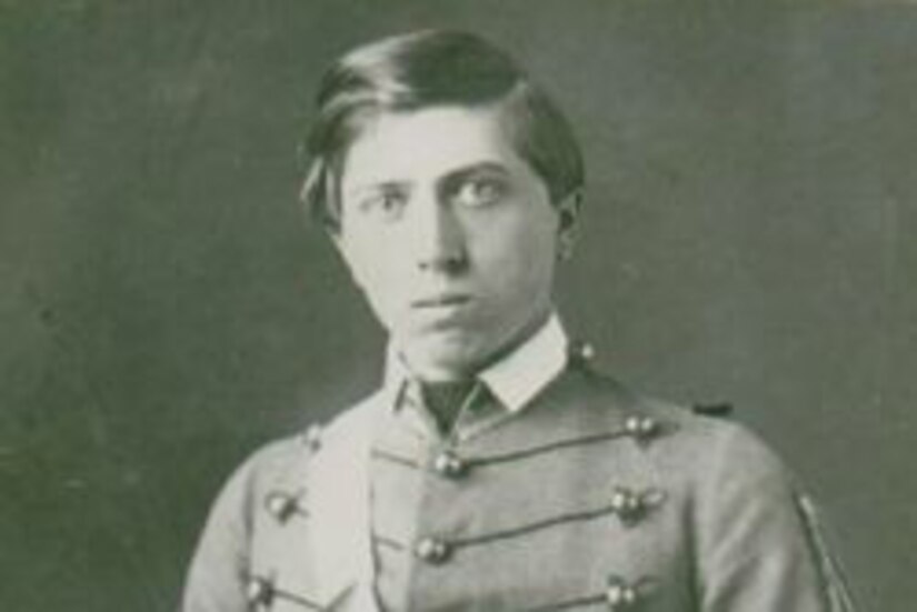 A young Civil War soldier in dress uniform looks at the camera as he holds a sword across his body.