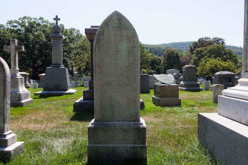 A large headstone in a graveyard reads “Brevet Lt. Colonel Alonzo H. Cushing.” Other headstones are spaced out around it.