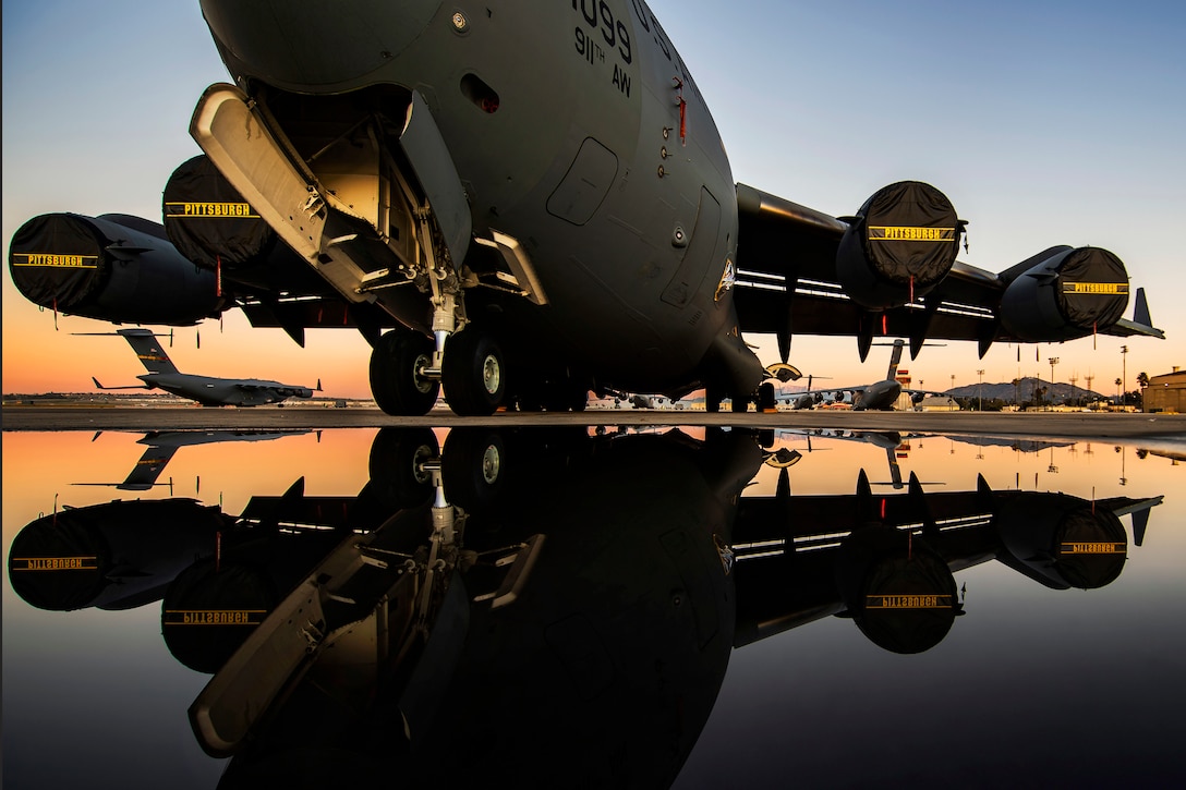 An aircraft sits on a flightline, the surface of which shows the plane's reflection.