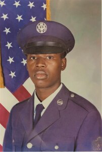 Official basic military portrait of a young man in U.S. Air Force dress blues with cover, posed in front of the American Flag.