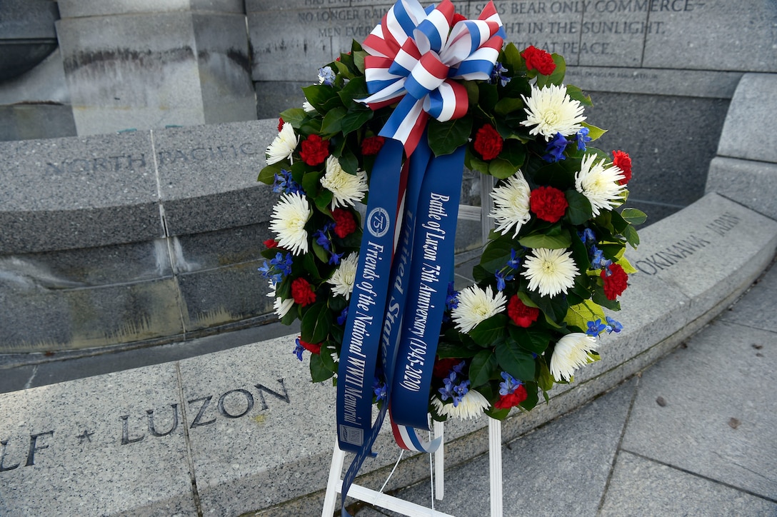 A floral wreath adorned with banners that read “Battle of Luzon 75th Anniversary,” “United States,” and “Friends of the National WWII Memorial” sits in front of a stone memorial that reads “Luzon.”