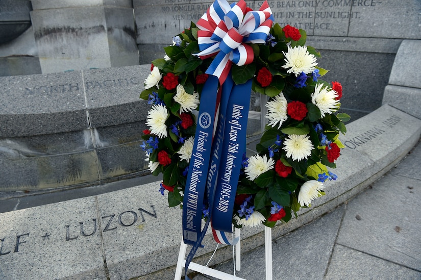 A floral wreath adorned with banners that read “Battle of Luzon 75th Anniversary,” “United States,” and “Friends of the National WWII Memorial” sits in front of a stone memorial that reads “Luzon.”