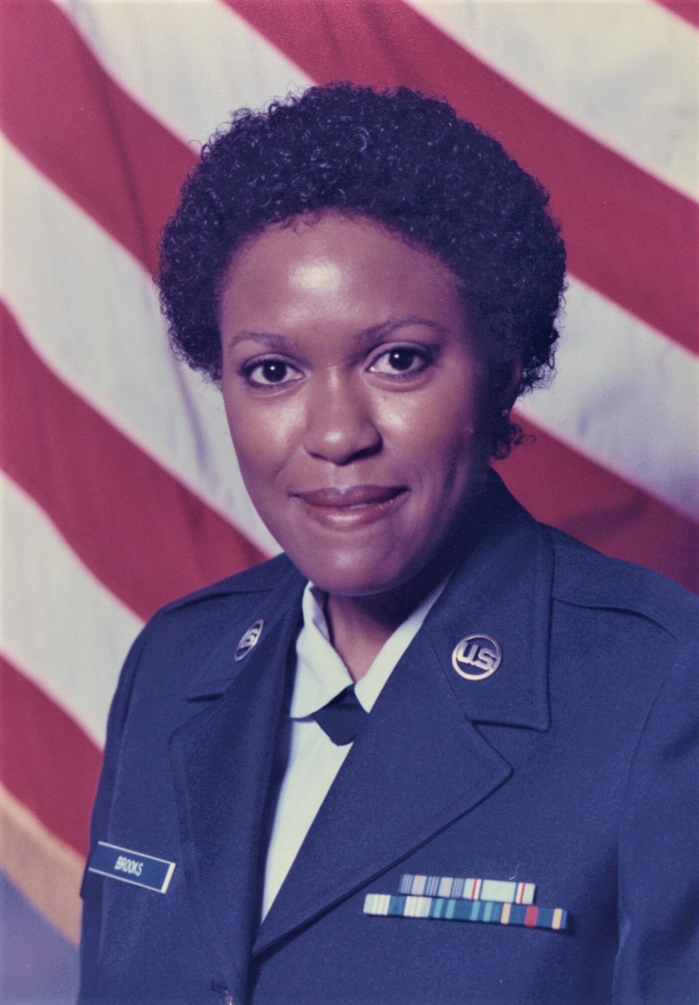 Official military  portrait of a young lady in dress blues posed in front of the American Flag
