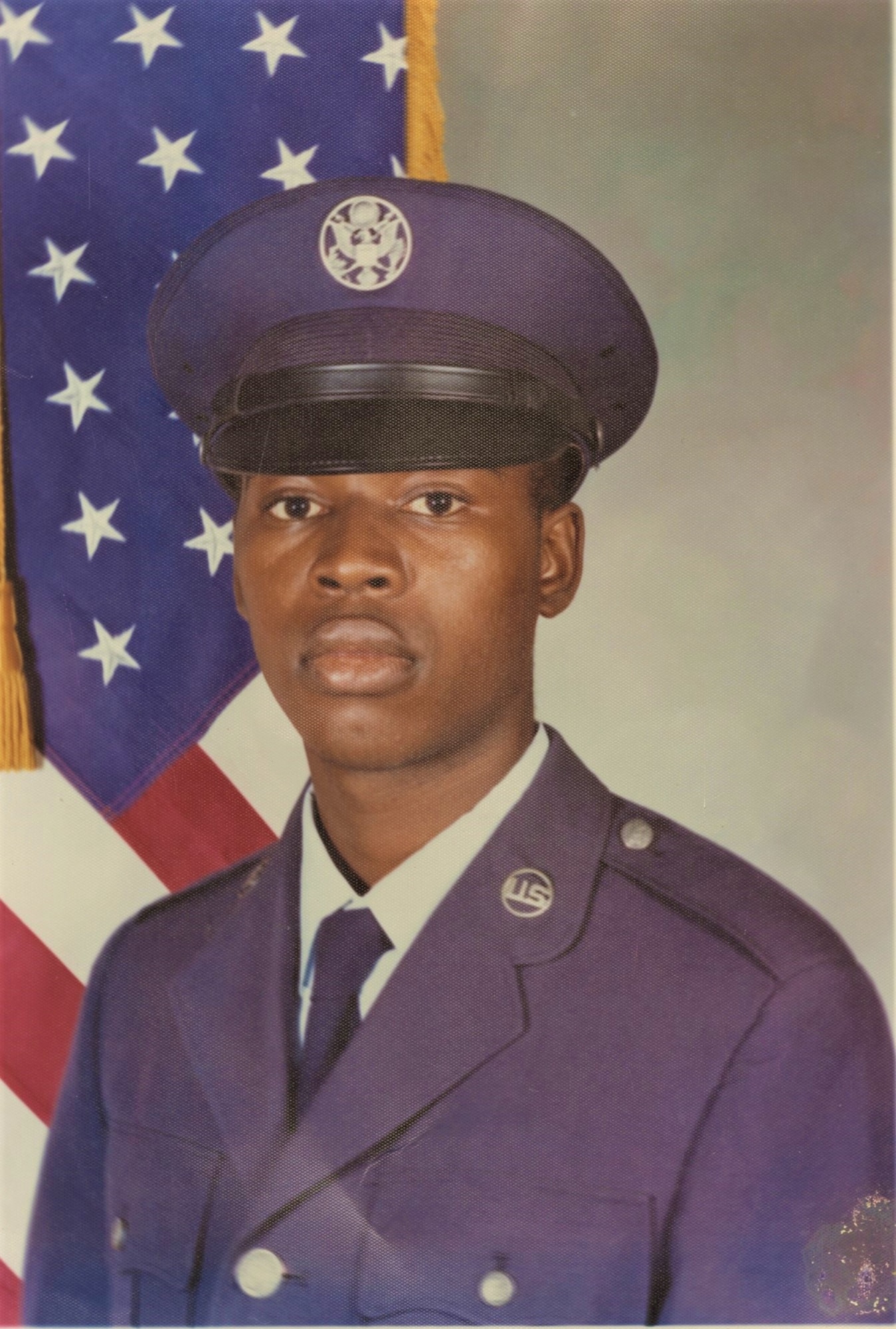 Official basic military portrait of a young man in U.S. Air Force dress blues with cover, posed in front of the American Flag.
