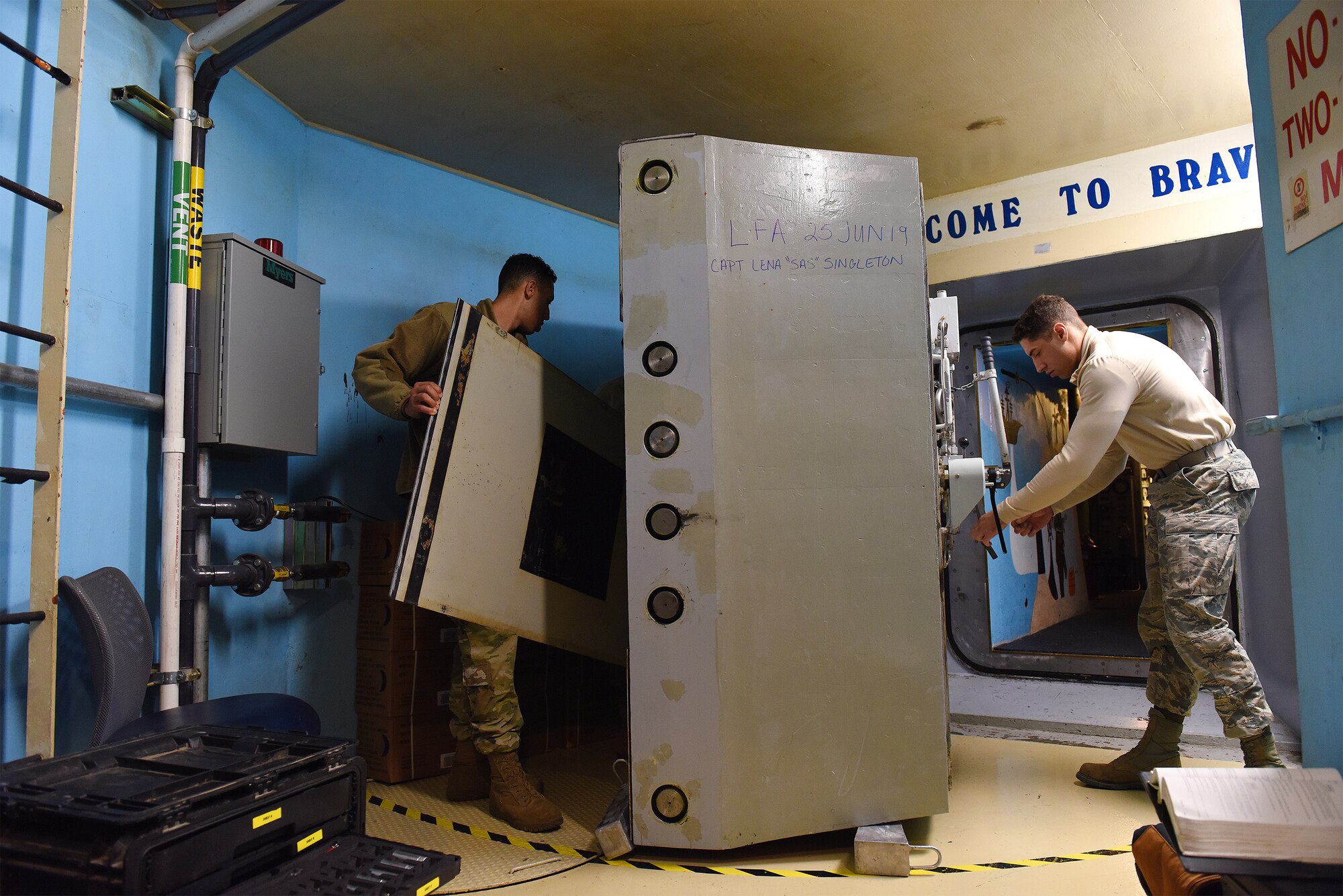 Airman 1st Class and Senior Airman perform maintenance on a launch control center blast door