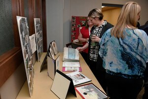 three women in front of table with posters and binders, one looks at the binders