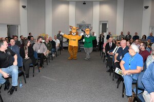 a yellow and green shirt mascot walk down the isle in the audience