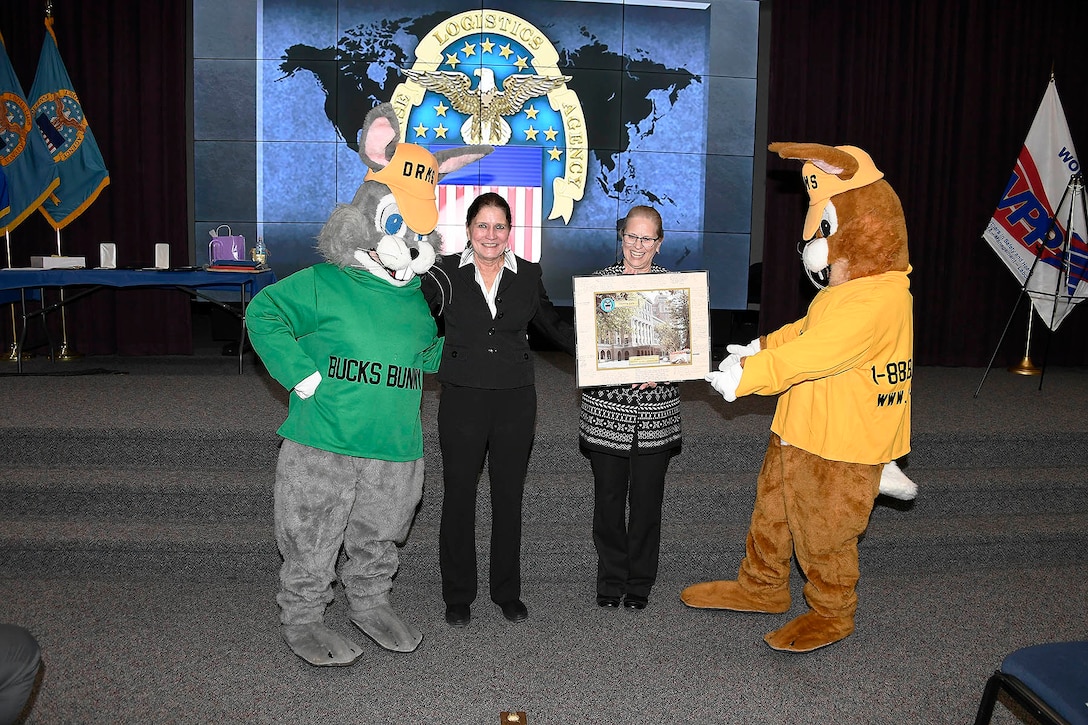 Mascots stand with Sherry Low and lady holding a picture