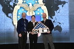 Two men and a woman stand on stage with a flag in a box