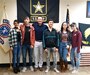 Three young women and three men standing in front of a recruiting guidon, an Army flag, and an American flag.