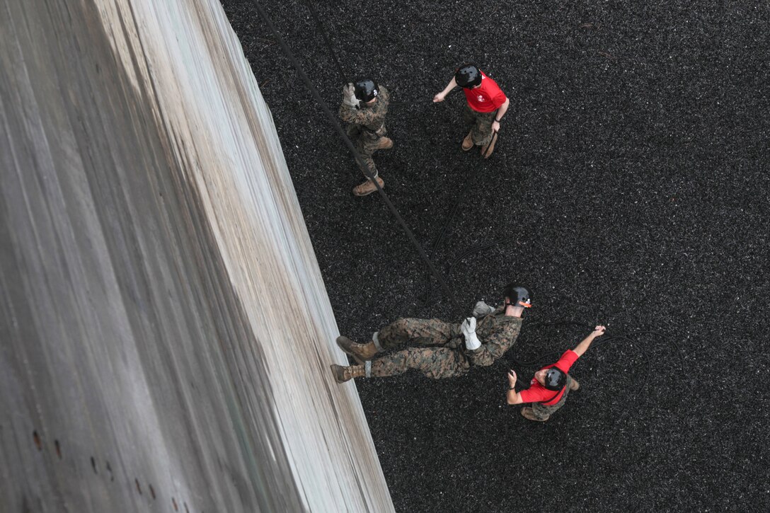 Marine Corps recruits use ropes to go down a wall.