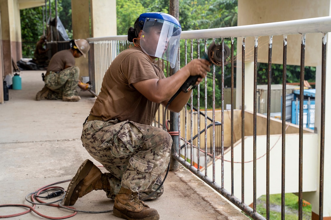 Sailors wearing protective headwear use tools to work on metal guardrails.