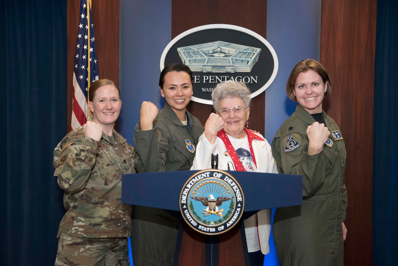 Three service members and a civilian flex their biceps behind a lectern.