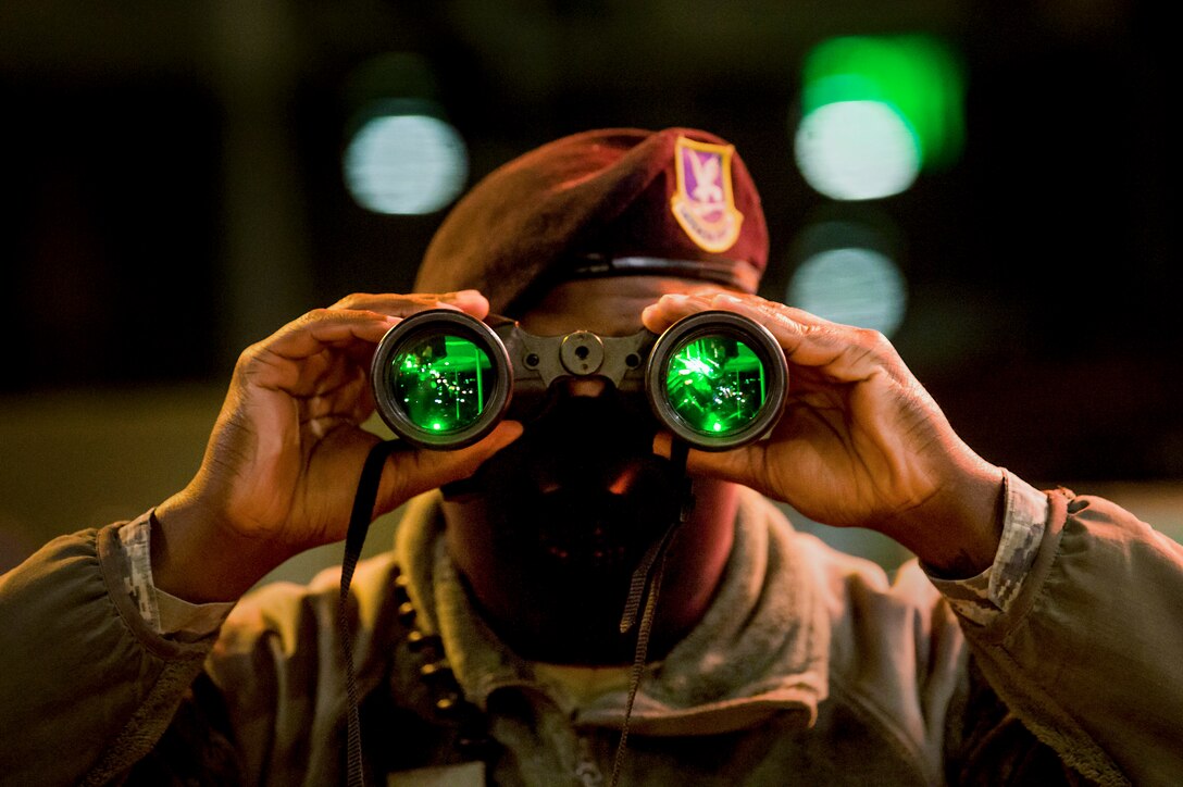 An airman looks through binoculars with green lenses at night.