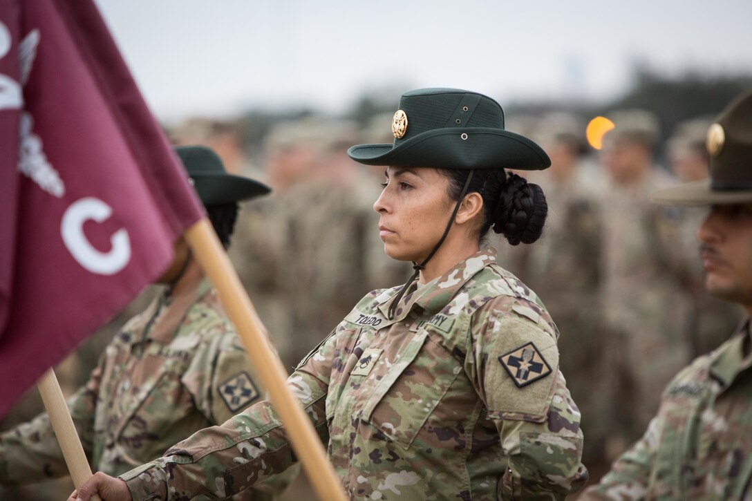 A soldier holds a flag while standing at attention during a ceremony.