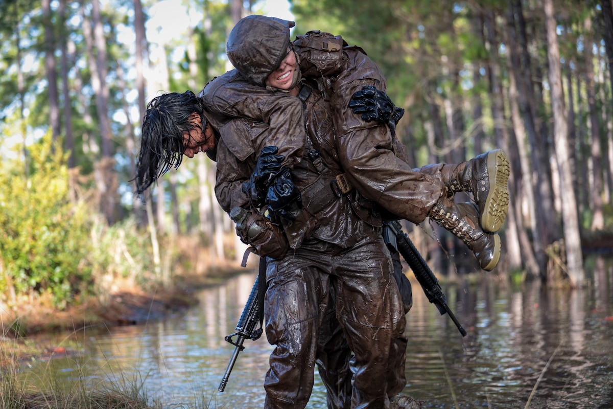 A Marine carries another Marine over her shoulder through a muddy swamp.