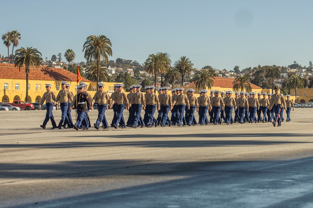 Marines in dress uniforms  march in formation during their graduation ceremony.