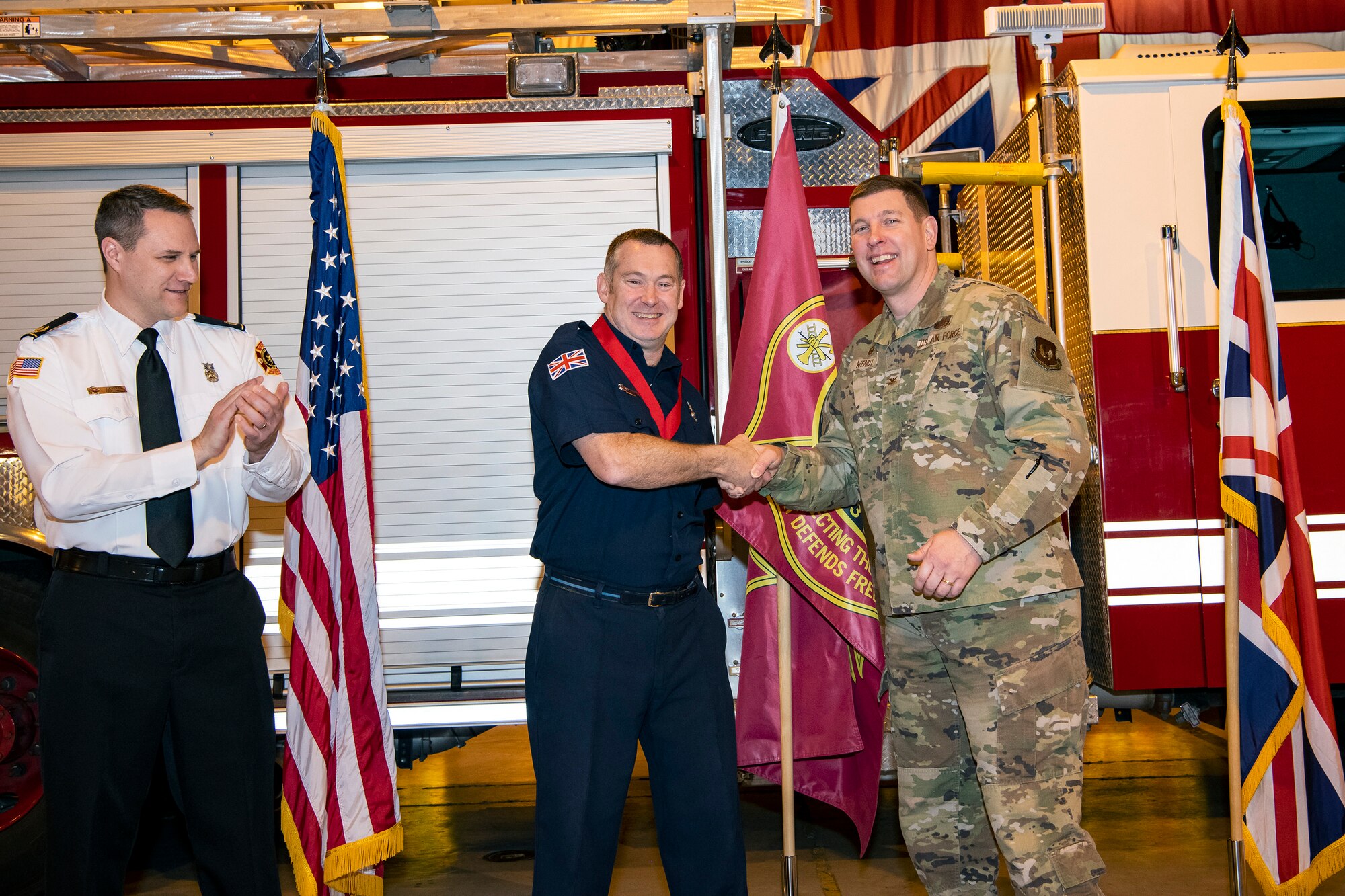 Robert Smith, center, 423rd Civil Engineer Squadron firefighter, receives a coin from Col. Kurt Went, 501st Combat Support Wing commander at RAF Alconbury, Dec. 20, 2019. Smith was recognized for exemplary lifesaving abilities under extreme pressure and clarity of mind for actions performed on August 21st. Smith administered CPR to his wife Karen for 17 minutes until paramedics arrived at his home. (U.S. Air Force photo by Senior Airman Eugene Oliver)