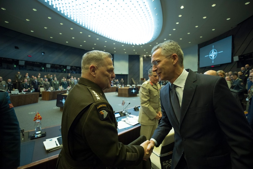 A person in a suit walks among military officers, shaking hands.