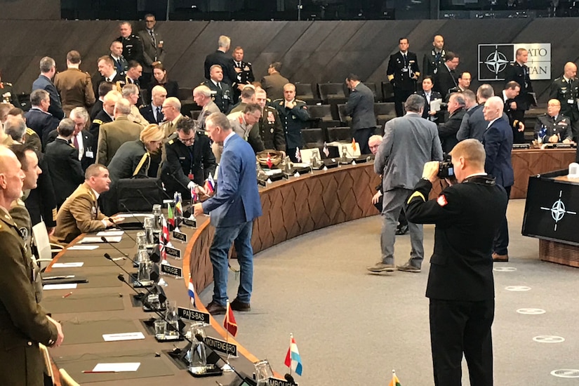 Military officers from various nations gather in a large meeting room.