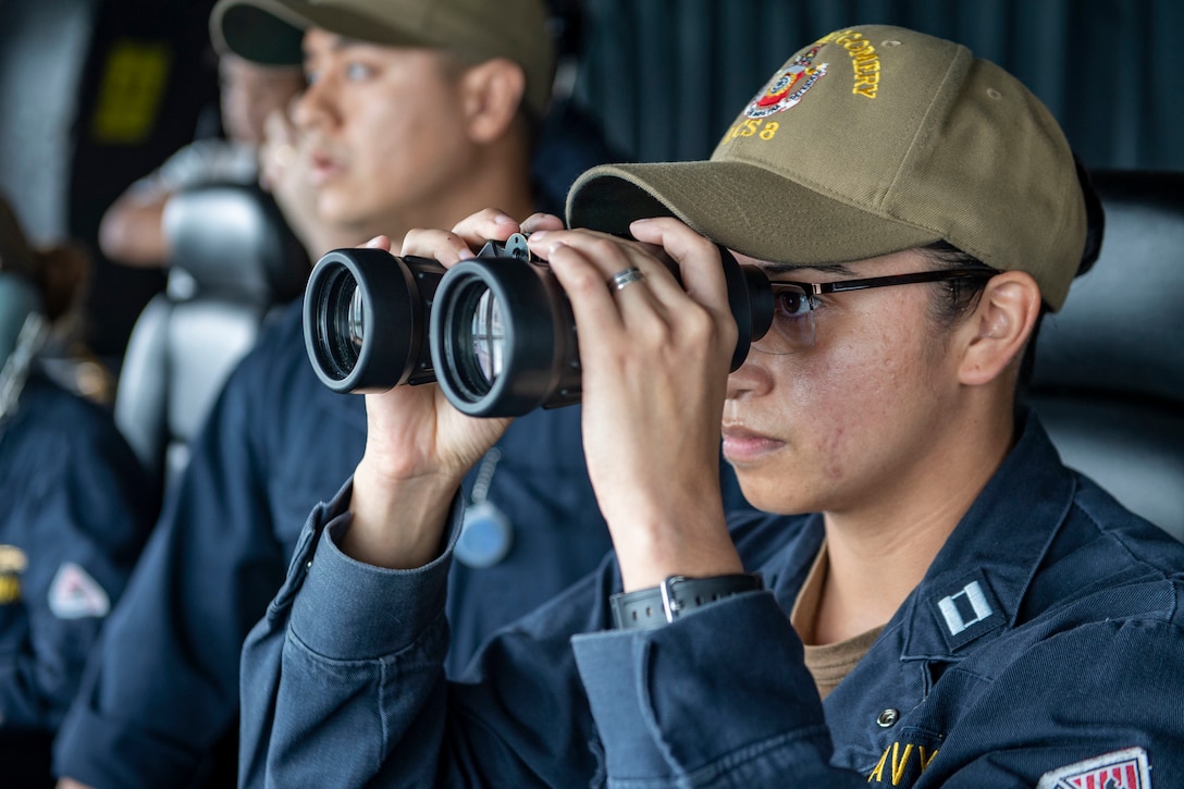 A sailor looks through binoculars.