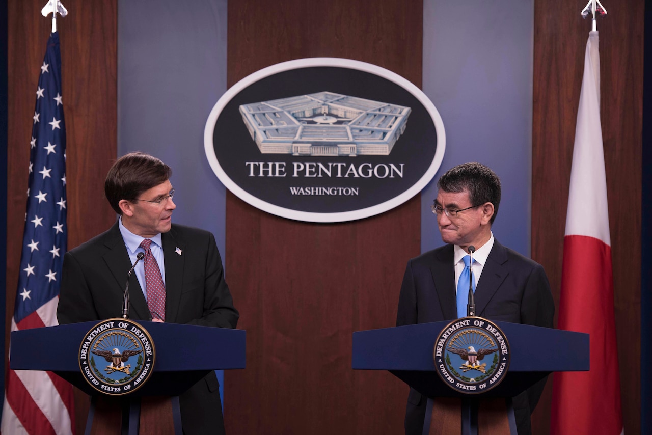 Two men stand at separate podiums during a news conference..