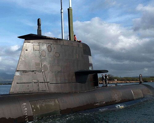 Two Sailors stand on top of a Collins-class guided missile submarine while in port.