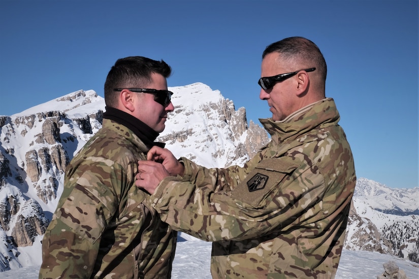 U.S. Army Reserve Master Sgt. Carlos Garcia, 2500th Digital Liaison Detachment, 7th Mission Support Command, pins rank on Staff Sgt. Wesley Cyrus, 2500th DLD, 7th MSC, in a mountain-top promotion ceremony after his unit used snowshoes to summit Monte Specie during winter survival training with the Italian Army´s 6th Alpine Regiment during exercise Alpine Rock in Toblach, Italy, January 11, 2020. Fifteen Soldiers from the 2500th participated in the winter survival training that emphasized small-unit tactical interoperability.