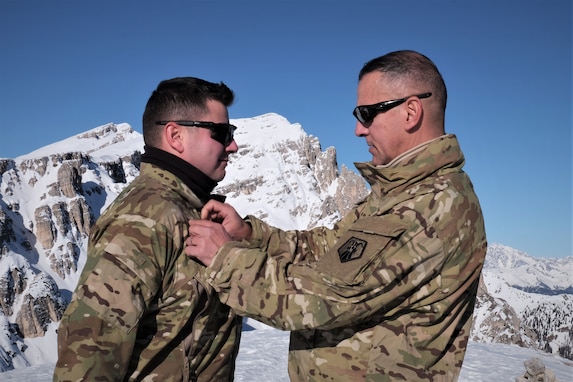 U.S. Army Reserve Master Sgt. Carlos Garcia, 2500th Digital Liaison Detachment, 7th Mission Support Command, pins rank on Staff Sgt. Wesley Cyrus, 2500th DLD, 7th MSC, in a mountain-top promotion ceremony after his unit used snowshoes to summit Monte Specie during winter survival training with the Italian Army´s 6th Alpine Regiment during exercise Alpine Rock in Toblach, Italy, January 11, 2020. Fifteen Soldiers from the 2500th participated in the winter survival training that emphasized small-unit tactical interoperability.