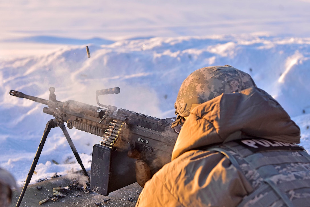 An airman fires a machine gun in a snowy mountainous area.