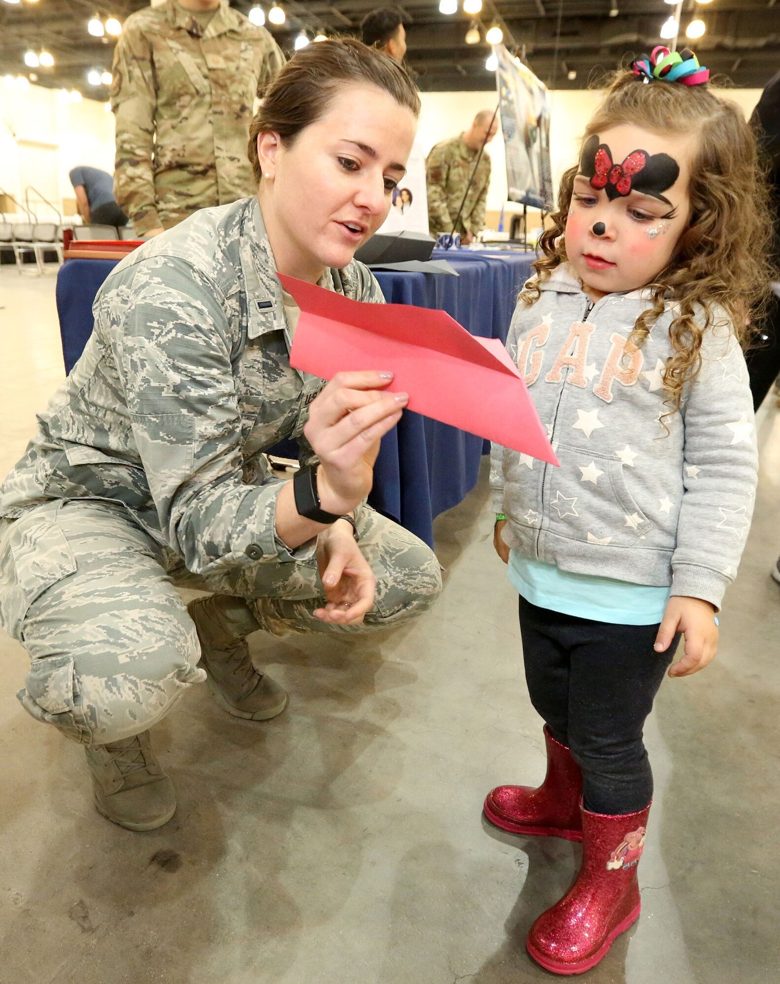 Airman showing young girl a paper airplane.