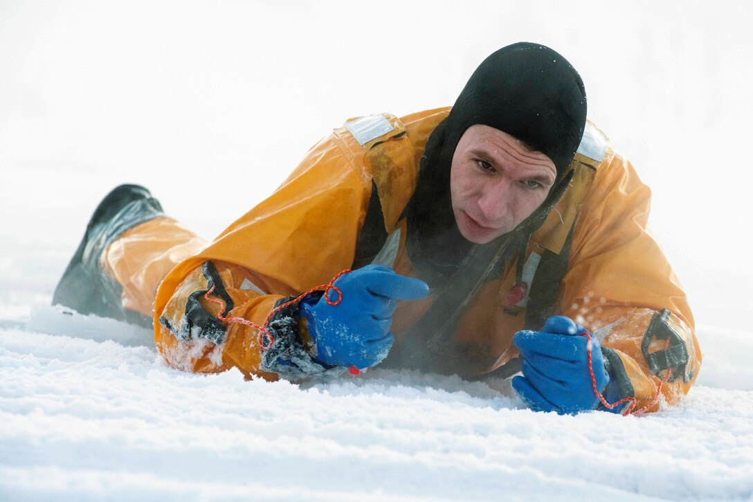 An airman lays on ice in a yellow suit during training.