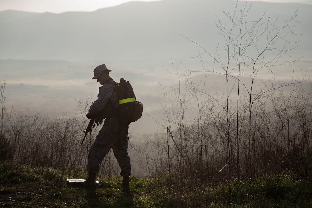 A service member with a pack on his back stands on a foggy hill holding a rifle.