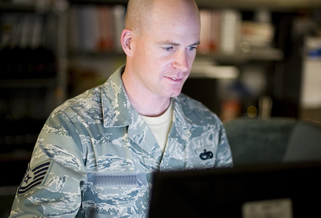 An Air Force technical sergeant looks at a computer screen, Name tape is digitally altered to protect his identity.