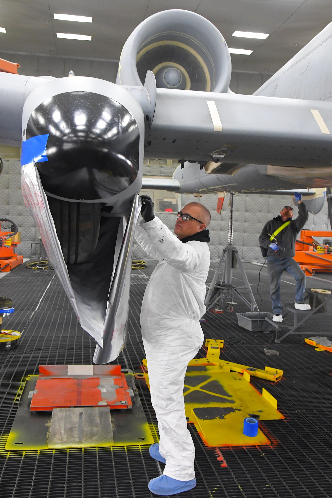 A technician is using a placing a cover on part of the wing of an A-10 aircraft located inside a lighted depaint facility.