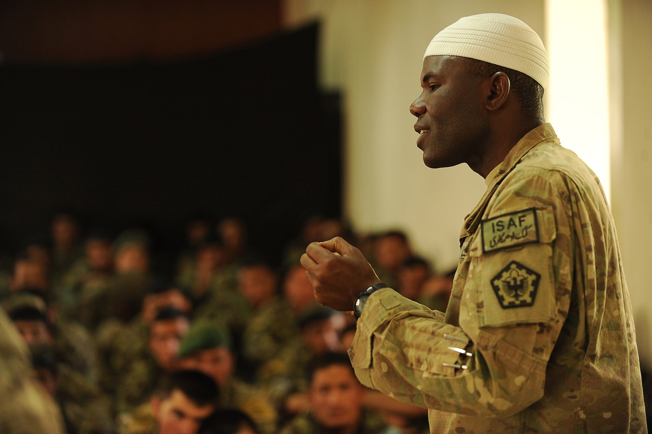 A chaplain in military uniform addresses a room full of military personnel.