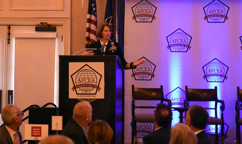 Woman standing at a lectern speaks and gestures.