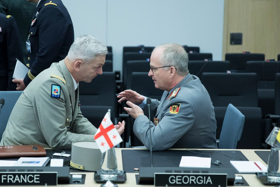Two men wearing military uniforms are deep in conversation.