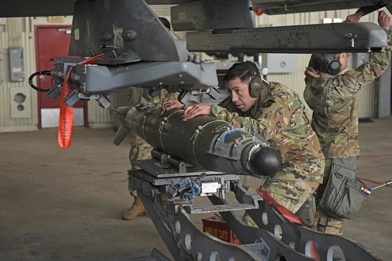 An airman crouched in uniform works on an aircraft.