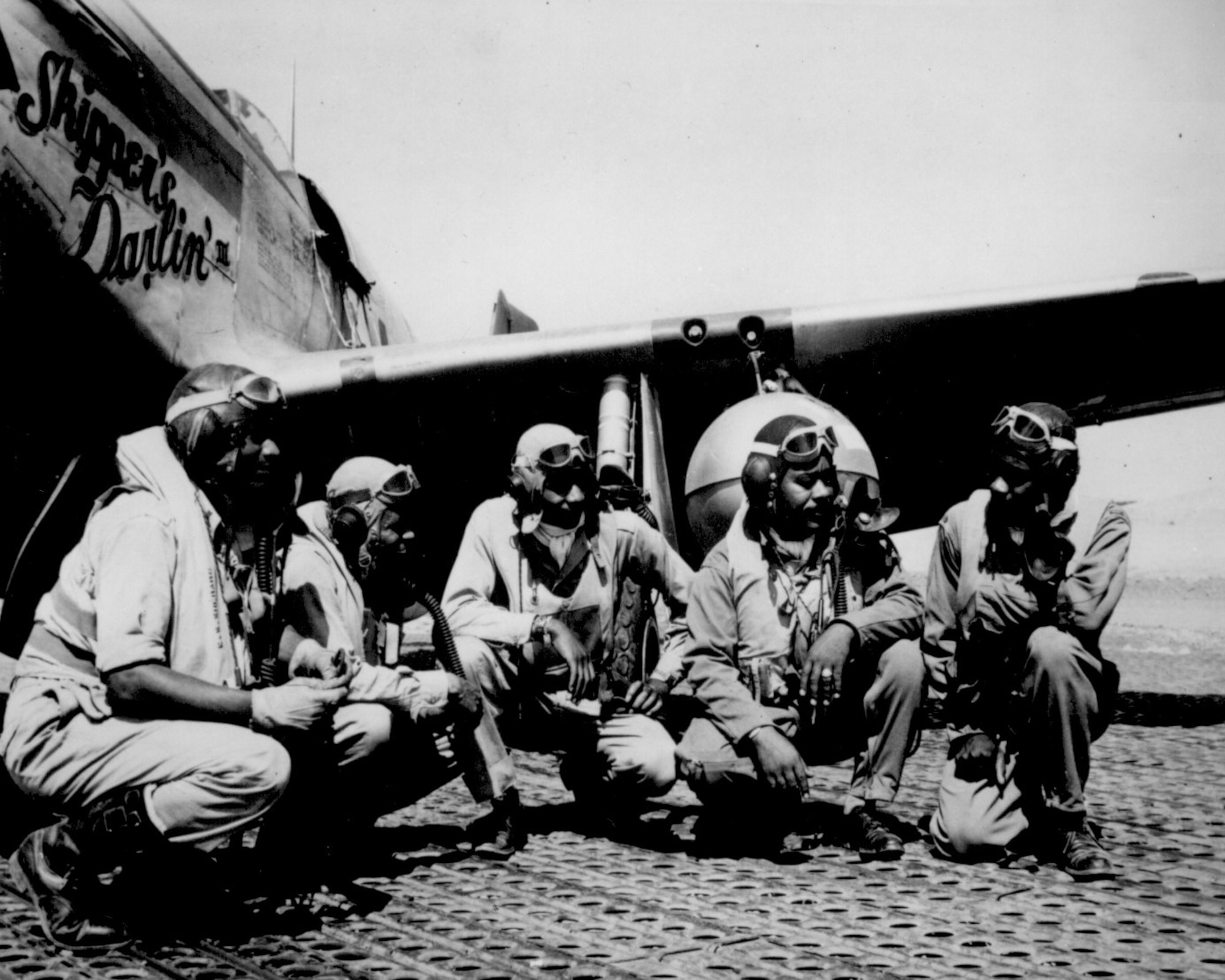 Fliers of a P-51 Mustang Group of the 15th Air Force in Italy talk in the shadow of one off the Mustangs they fly, August 1944. Left to right, Lt. Dempsey W. Morgan Jr., Lt. Carroll S. Woods, Lt. Robert H. Nelson Jr., Capt. Andrew D. Turner, and Lt. Clarence P. Lester.