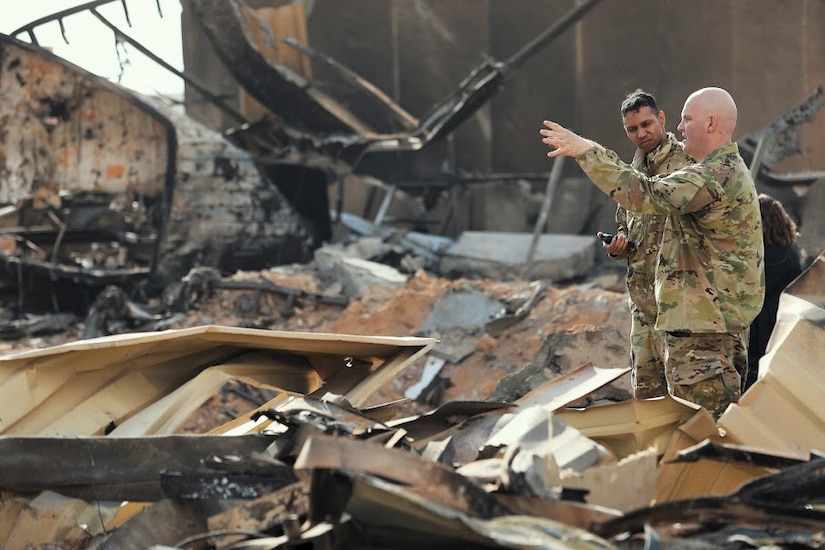 Two soldiers surrounded by a pile of charred metal debris.